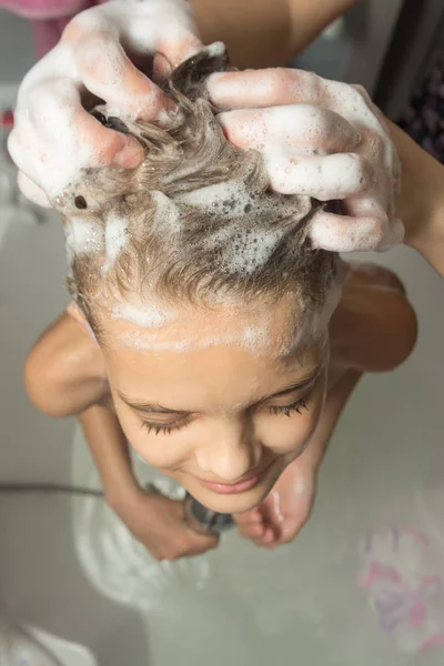 Mamá enjabonó el pelo largo del niño con champú y los masajes, la vista superior — Foto de Stock