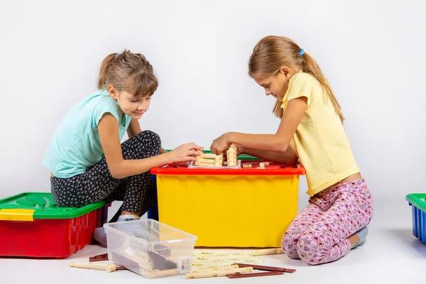 Две девушки собирают дом на коробке с игрушками, глядя в инструкции — стоковое фото