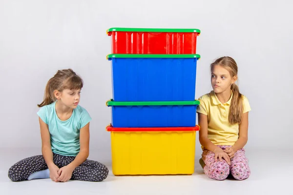 Two girls look at each other hiding behind large plastic boxes in the middle between them — Stock Photo, Image