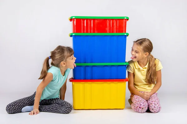 Две девушки подглядывают с разных сторон больших пластиковых коробок и показывают друг другу свои языки — стоковое фото