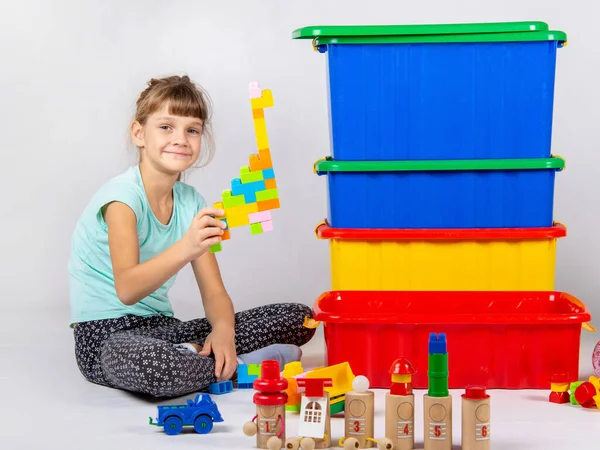 Lány játszik játékok, nagy műanyag dobozok állnak a közelben — Stock Fotó