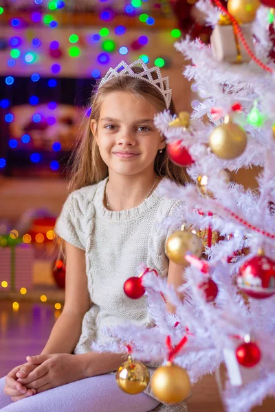 Hermosa chica se sienta junto a un árbol de Navidad blanco — Foto de Stock