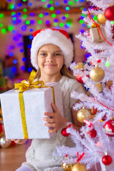 Chica sentada junto al árbol de Navidad con grandes regalos en sus manos —  Fotos de Stock