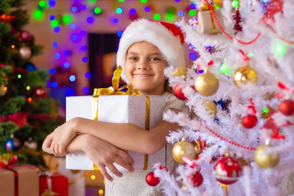クリスマスツリーの女の子は彼女の手に大きな贈り物を持っています — ストック写真