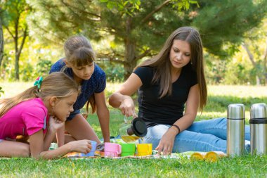 Family on a picnic, girl pours tea in glasses, children watch clipart