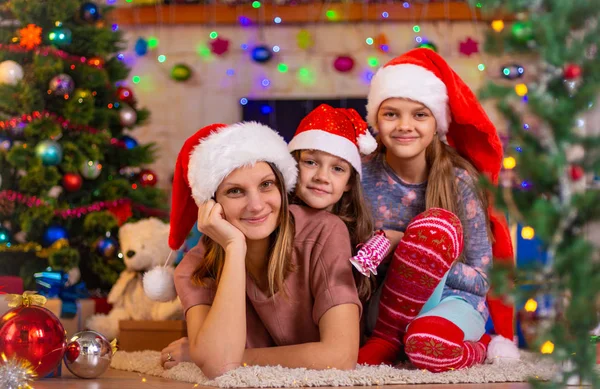 Mamá y dos hijas yacen en el suelo de un árbol de Navidad —  Fotos de Stock