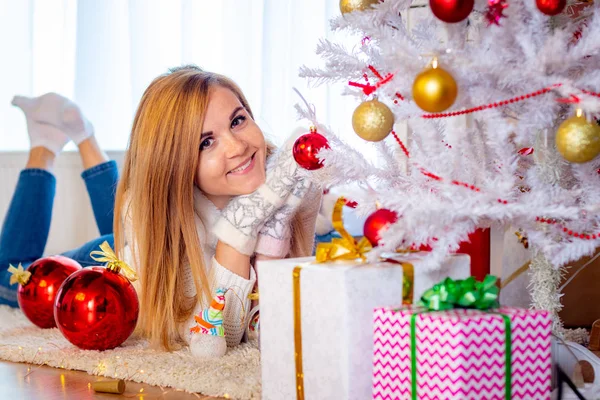 Una joven se acuesta en el árbol de Navidad y se ve feliz en el marco —  Fotos de Stock