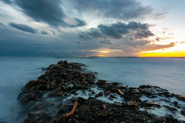 Морской закат после заката, на переднем плане волнолом из камней — стоковое фото