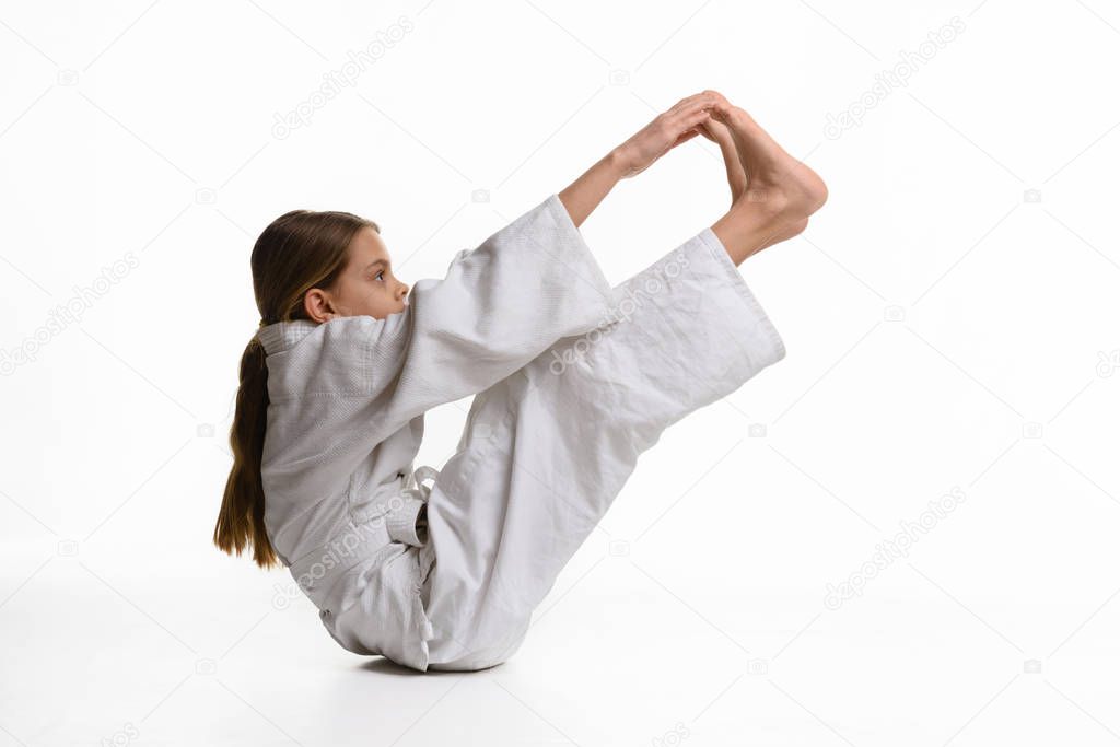 A girl in a sports kekogi reaches her hands at her feet, waving a stretch