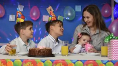 Çocuklar ve anneleri şenlik masasında otururken konuşurlar.