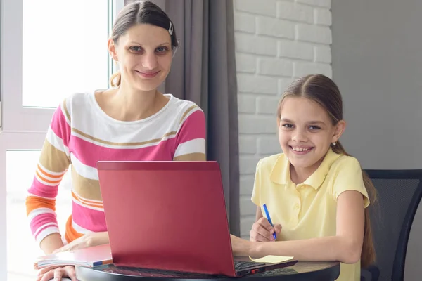 快乐的女孩和妈妈笑着看着镜框 坐在桌旁做作业 — 图库照片