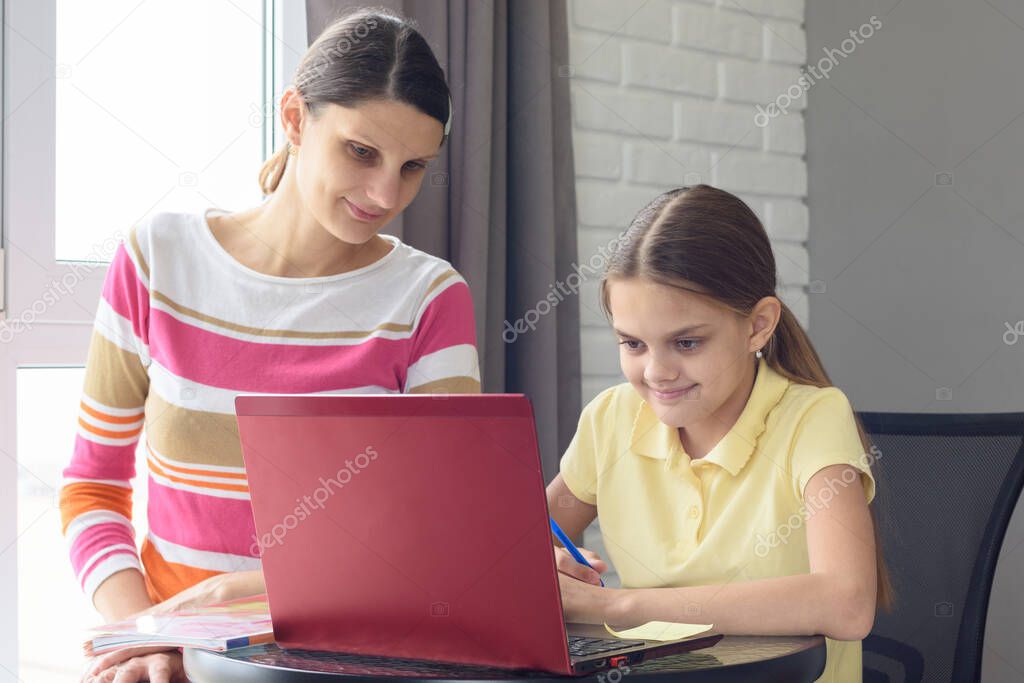 A girl and a girl are sitting at a table and browsing web pages in a laptop