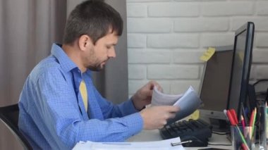 Genç bir adam evde bilgisayar başında çalışıyor, belgeleri inceliyor.