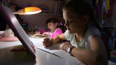Kız kardeşler gece geç saatlere kadar ödev yapıyor, masada oturuyor, içlerinden biri uyumak istiyor ve esniyor.