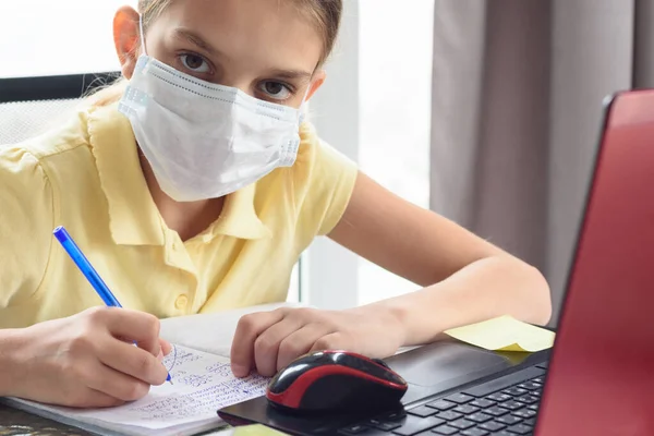 The sick girl in self-isolation mode does her homework and looked into the frame.