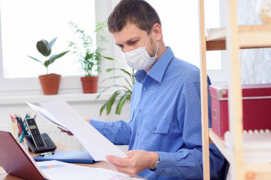 Koruyucu tıbbi maske takan ofis çalışanı ofiste evraklarla çalışıyor.
