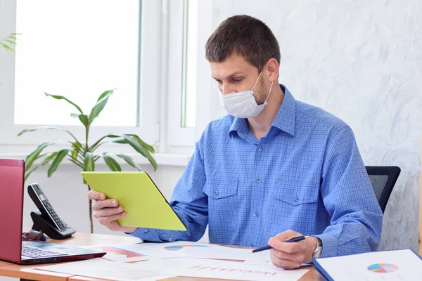 Bir ofis çalışanı video bağlantısıyla iletişim kuruyor. Yüzünde tıbbi maske var.