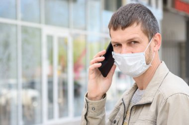 Mağazanın arka planında cep telefonu olan tıbbi maskeli bir adamın portresi, çerçeveye bakıyor.