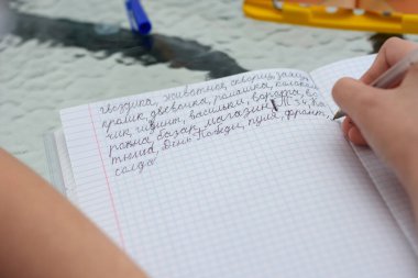 Çocuk mektupları doğru yazmayı öğrenir ve bir deftere Rusça çeşitli kelimeler yazar.