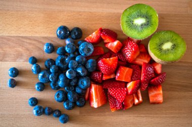 Ahşap bir masada çilek, yabanmersini ve kivi.