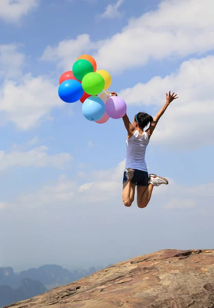 Young woman jumping with colorful balloons — Stock Photo, Image
