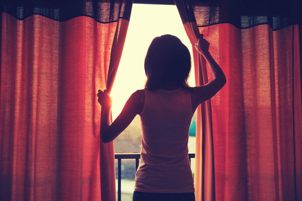 young woman opening curtains