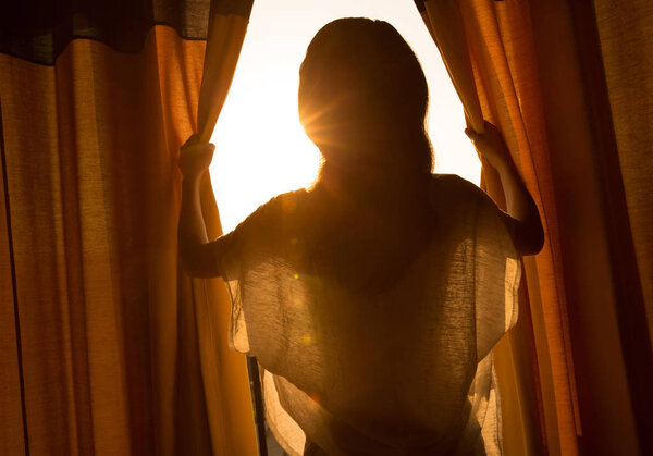 young woman opening curtains