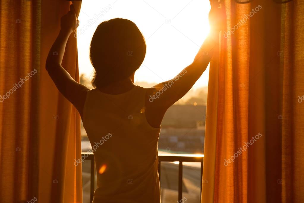 young woman opening curtains