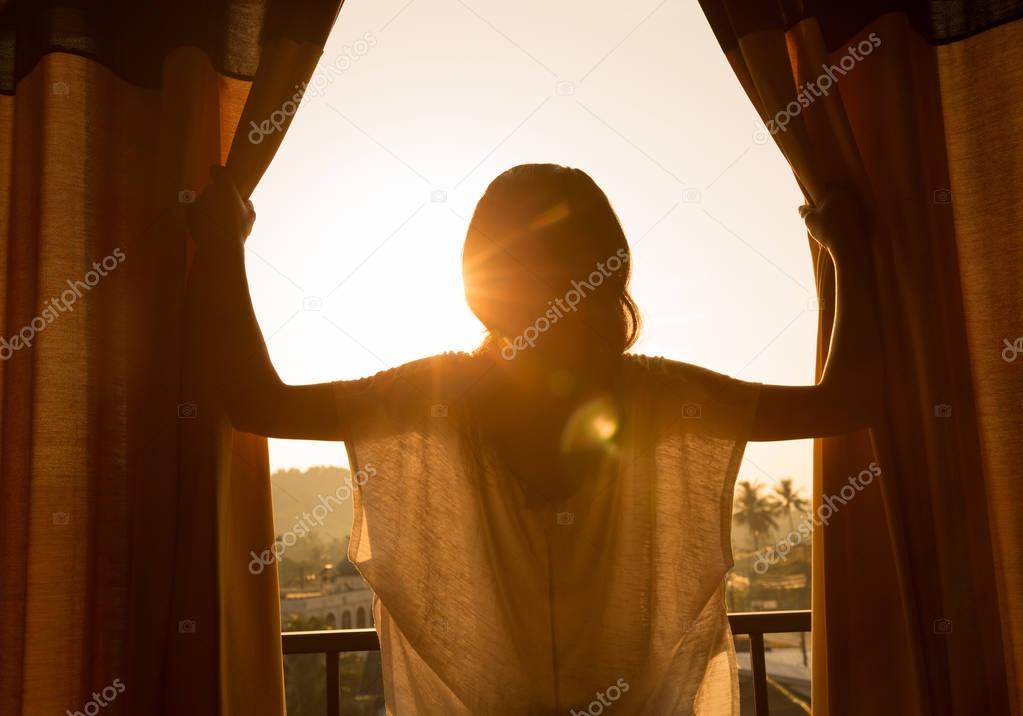 young woman opening curtains