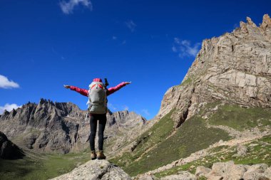 Sırt çantalı genç bir kadın dağlarda yürüyüş yapıyor.