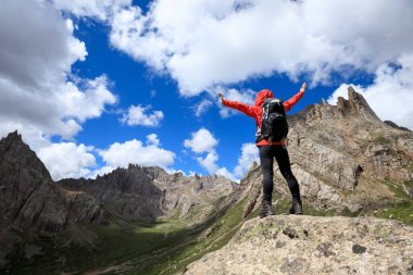 Sırt çantalı genç bir kadın dağlarda yürüyüş yapıyor.