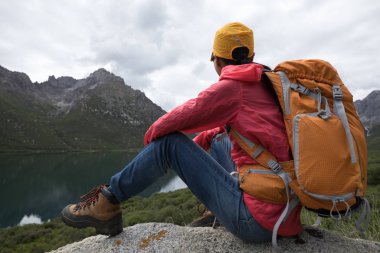 genç kadın backpacking lakeside kayalıklarda oturan manzarasının tadını çıkarın.