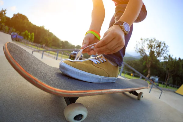 young woman skateboard tying shoelace at skatepark