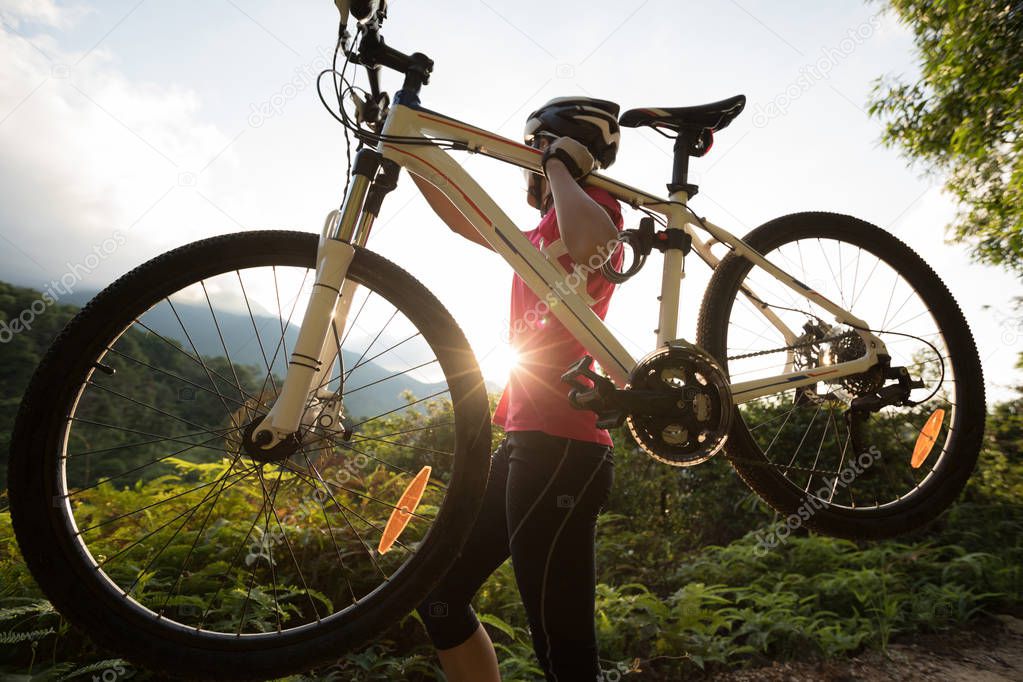 Young woman cyclist carrying bicycle on summer forest trail