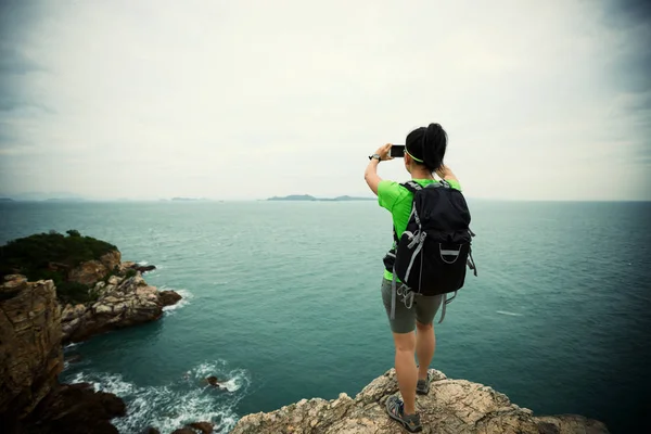 在海边悬崖上使用智能手机的年轻女子徒步旅行 — 图库照片