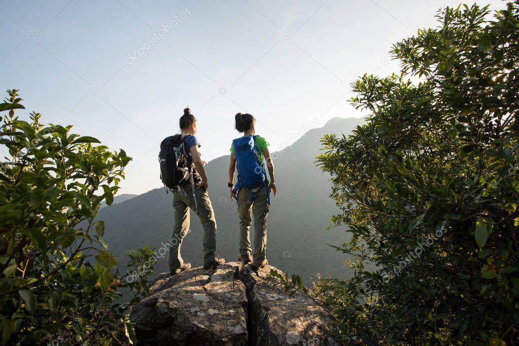 two young women backpackers standing on mountain edge in the sunrise