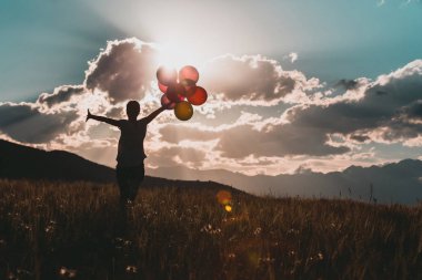 Çayır renkli balonlarla günbatımı sırasında çalışan genç kadın tezahürat