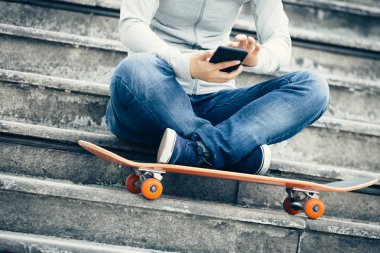 kaykay ile şehir merdivenlerde otururken Smartphone kullanarak kaykaycı