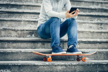 kaykay ile şehir merdivenlerde otururken Smartphone kullanarak kaykaycı