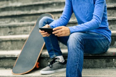 kaykay ile şehir merdivenlerde otururken Smartphone kullanarak kaykaycı