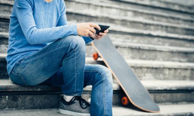 kaykay ile şehir merdivenlerde otururken Smartphone kullanarak kaykaycı