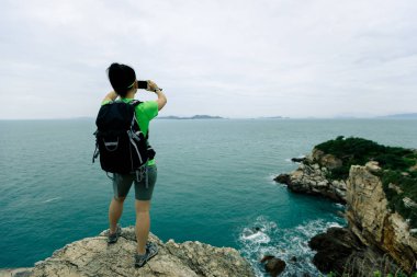 Genç kadın deniz cliff üzerinde Smartphone kullanarak uzun yürüyüşe çıkan kimse