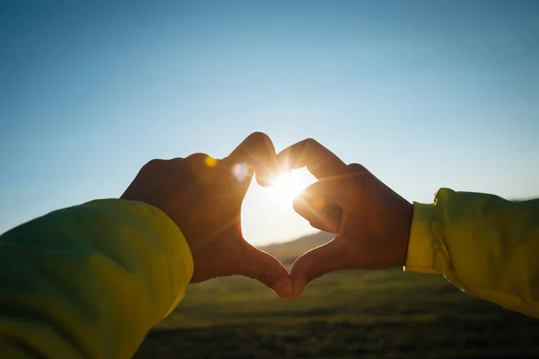 Human hands making Heart shaped sign over sunset sky