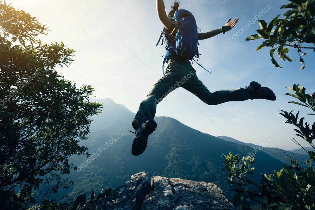 successful young woman backpacker jumping on cliff