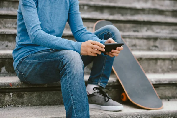 街の階段の上に座っている間はスマート フォンを使用してのスケートボーダー — ストック写真