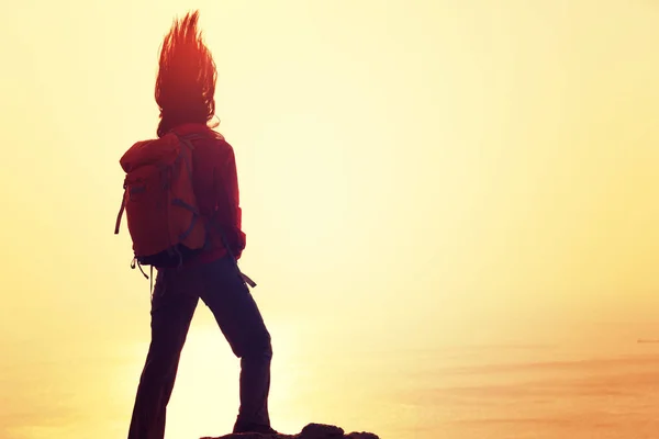 有背包的少妇站立在日出风的海岸 — 图库照片