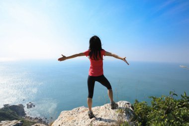 gündoğumu rüzgarlı sahil üzerinde uzanmış kollarıyla duran genç kadın
