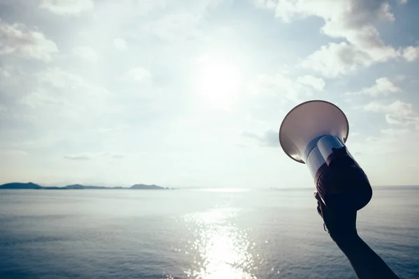 Hand hold megaphone against sea under sky background