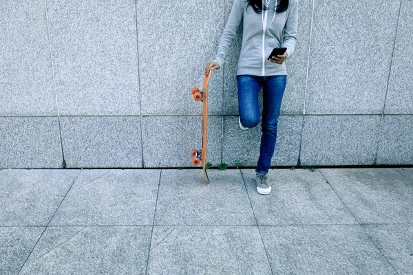 Θηλυκό Skateboarder Χρησιμοποιώντας Smartphone Ενώ Ακουμπά Στον Τοίχο Στην Πόλη — Φωτογραφία Αρχείου