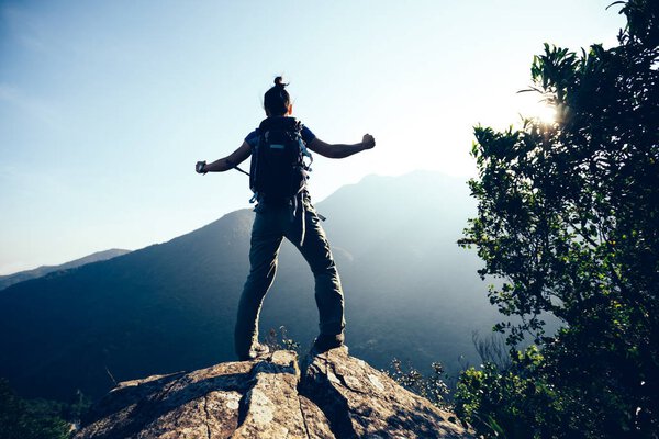 young woman backpacker standing on mountain top  with raised hands